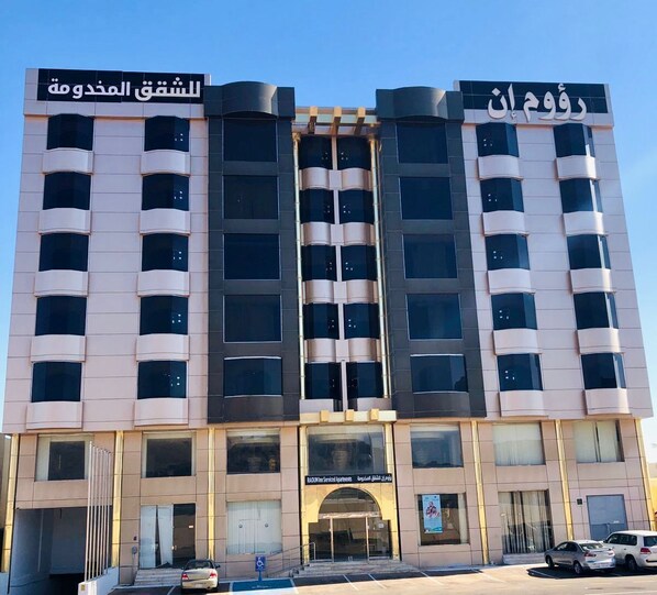 A multi-story building with a modern architectural design, featuring a central entrance with glass doors and a sign indicating it is a serviced apartment complex.