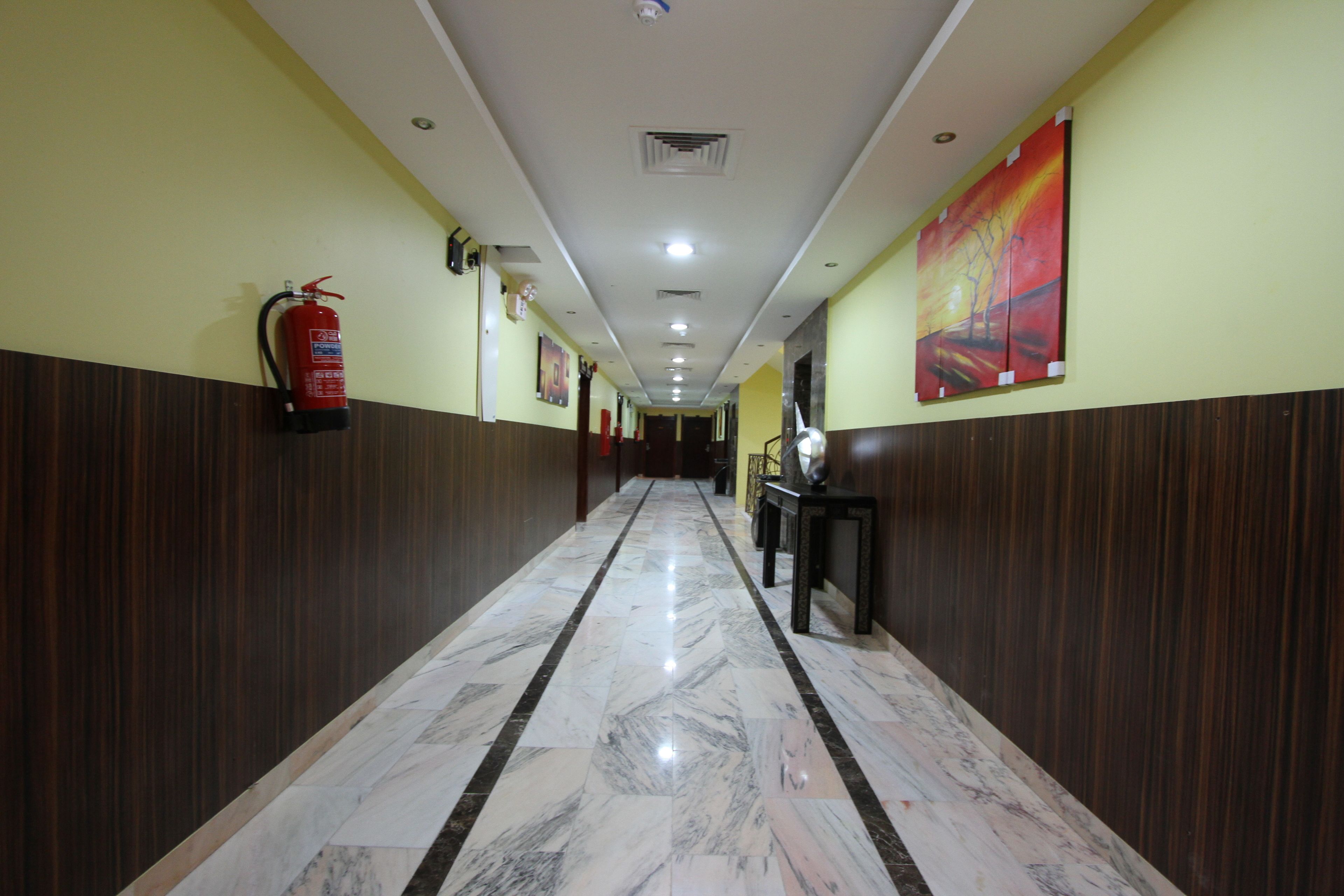A hallway with a marble floor, wooden paneling on the walls, a fire extinguisher, and a painting on the right wall.