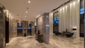 A spacious lobby with marble flooring, a reception desk, and a seating area with a modern chair and lamp.