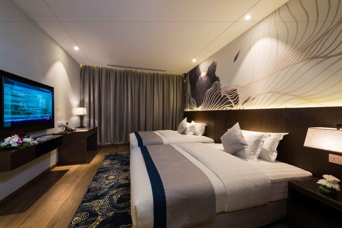 A hotel room with two beds, a TV, a desk, and a decorative wall.