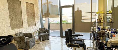 A modern salon with a marble floor, large windows, and a seating area with sofas.