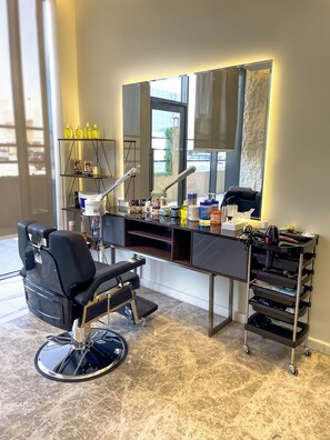 Un salon moderne avec un fauteuil noir, un grand miroir et divers produits de soins capillaires disposés sur des étagères.