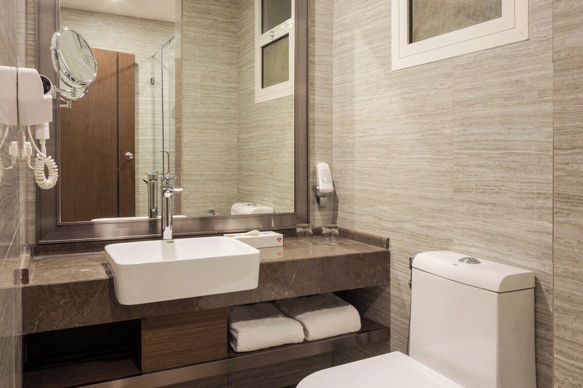 Ein modernes Badezimmer mit großem Spiegel, Waschbecken, Toilette und Handtuchhalter.