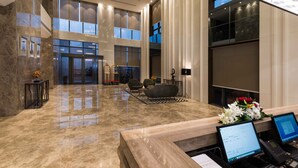 A spacious lobby with a marble floor, large windows, a reception desk, and seating area.