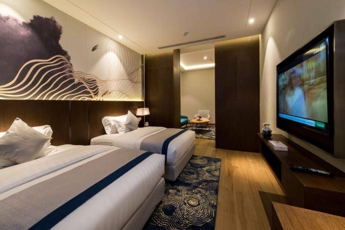 A hotel room with two beds, a television, a desk, and a wall art piece.