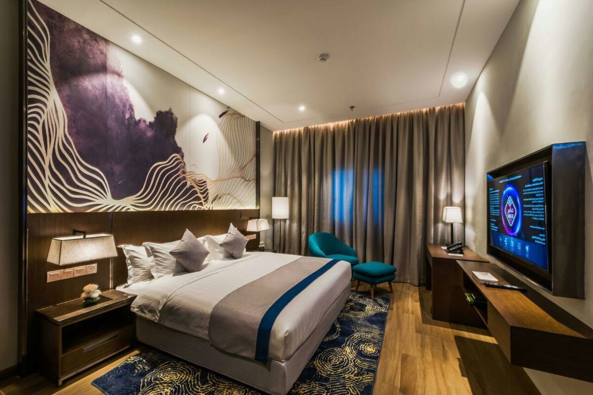 A modern hotel room with a large bed, a TV, a desk, and a chair.