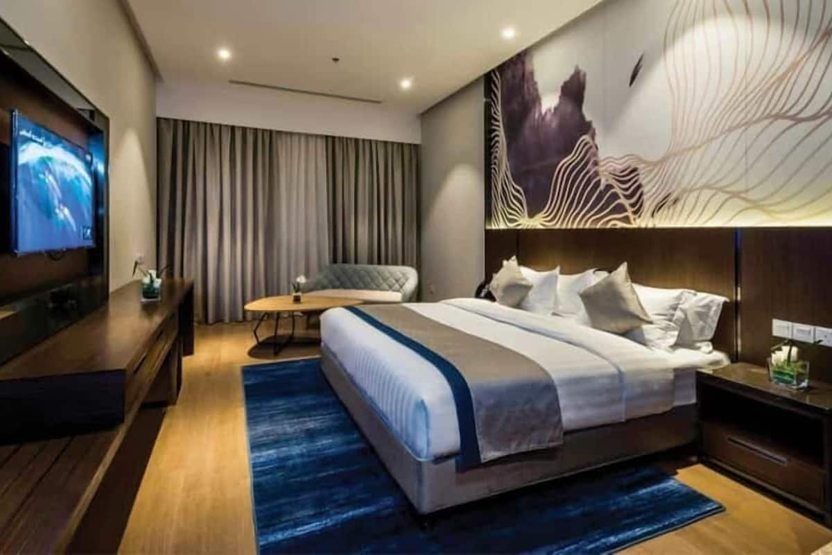 A modern hotel room with a large bed, a TV, a desk, and a chair.