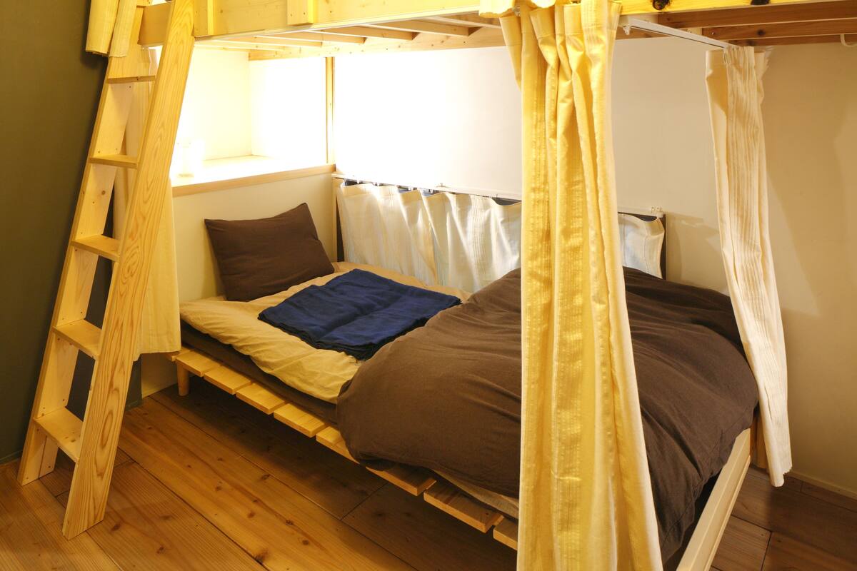 Un lit superposé avec une échelle en bois, une fenêtre avec des rideaux et une table de chevet.