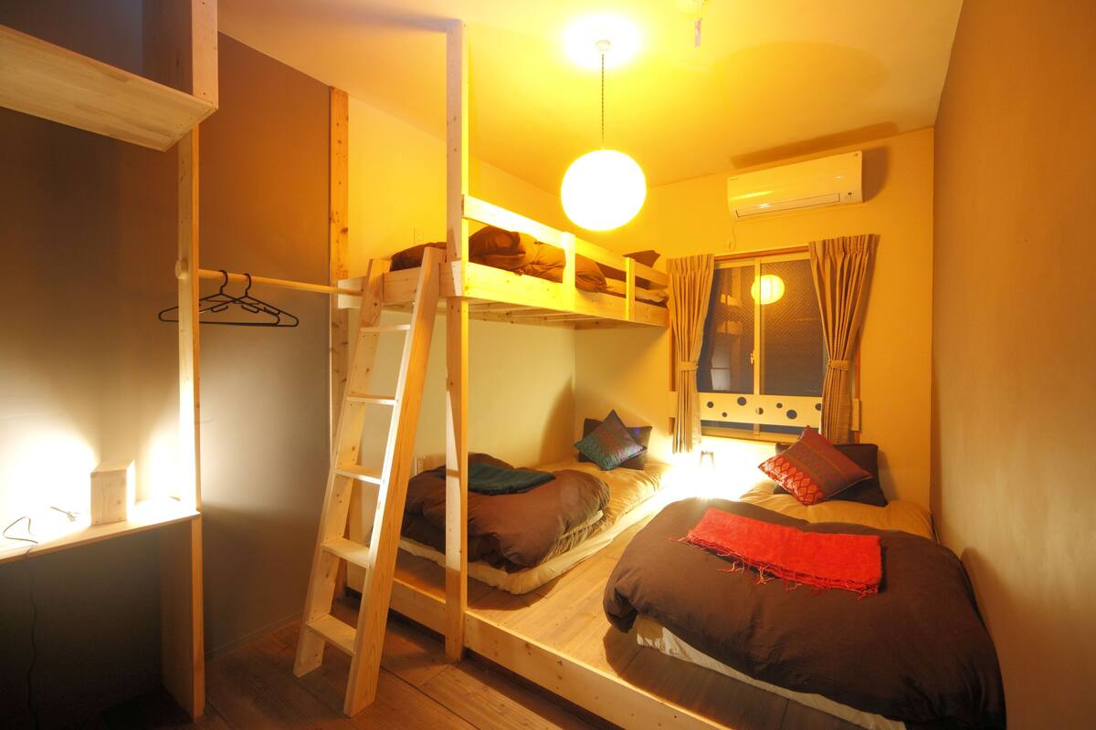 Une chambre de dortoir avec des lits superposés, une échelle, un bureau avec une chaise et une fenêtre avec des rideaux.