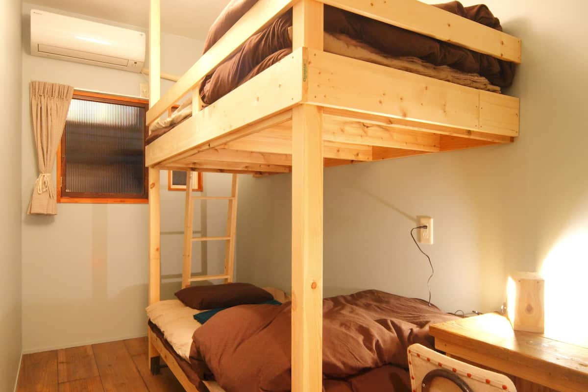 Une chambre avec un lit superposé, un bureau et une chaise, un plancher en bois et une fenêtre avec des rideaux.