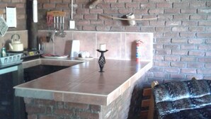 Een rustieke keuken met een bakstenen muur, een houten plafond en een klein eiland met een wit aanrecht.