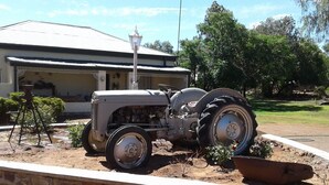 Een oude tractor geparkeerd voor een gebouw met een golfplaten dak.