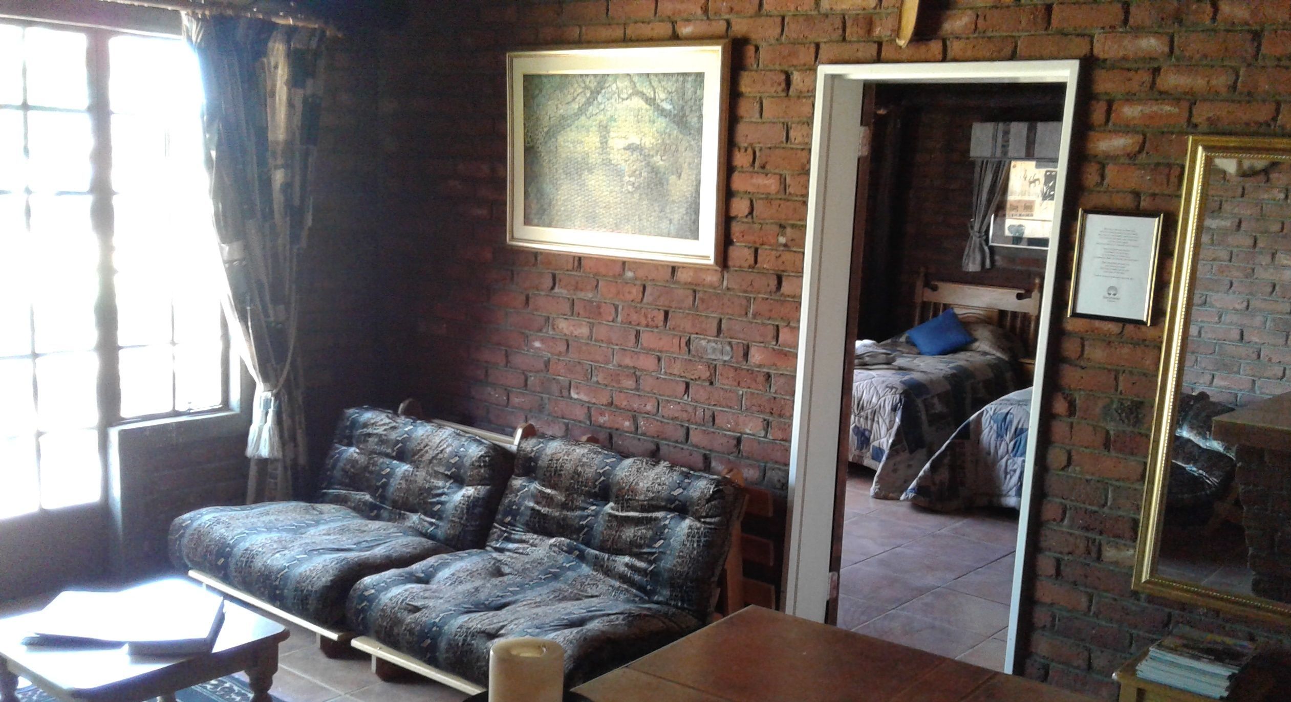 A room with a brick wall, a sofa, a table, and a mirror.