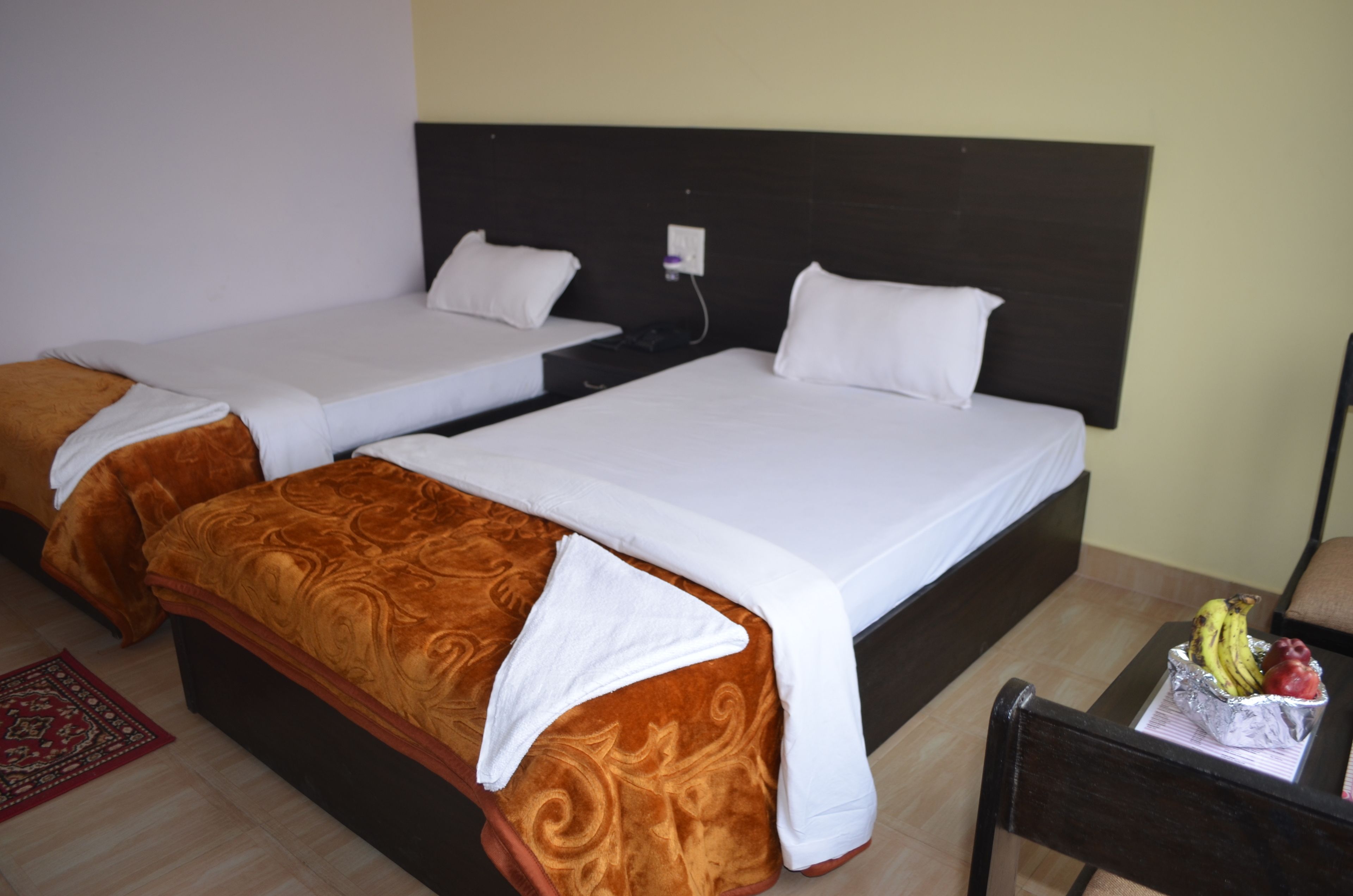 Habitación de hotel con dos camas, un cabecero de madera, una mesita con fruta y una alfombra roja.