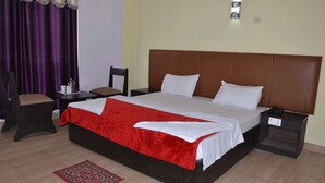 A hotel room with a large bed, a nightstand, a chair, and a red patterned rug. - Hotel Joshi (Siddharthanagar)