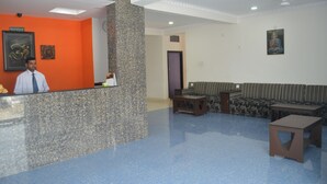 A reception area with a receptionist, a reception desk, a sofa set, and a small table. - Hotel Joshi (Siddharthanagar)