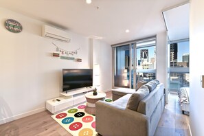 Een moderne woonkamer met een grote flatscreen televisie, een bank, een kleurrijk button-tapijt en een stadszicht door grote ramen.