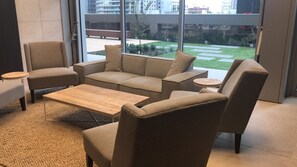 A modern living room with a beige sofa, two armchairs, a coffee table, and a small side table. Large windows offer a view of a courtyard with greenery and a building in the background. - Southern cross The fifth Apartment (Melbourne)