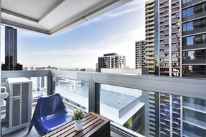 A balcony with a blue chair, a small potted plant, and an air conditioning unit. - Southern cross The fifth Apartment (Melbourne)