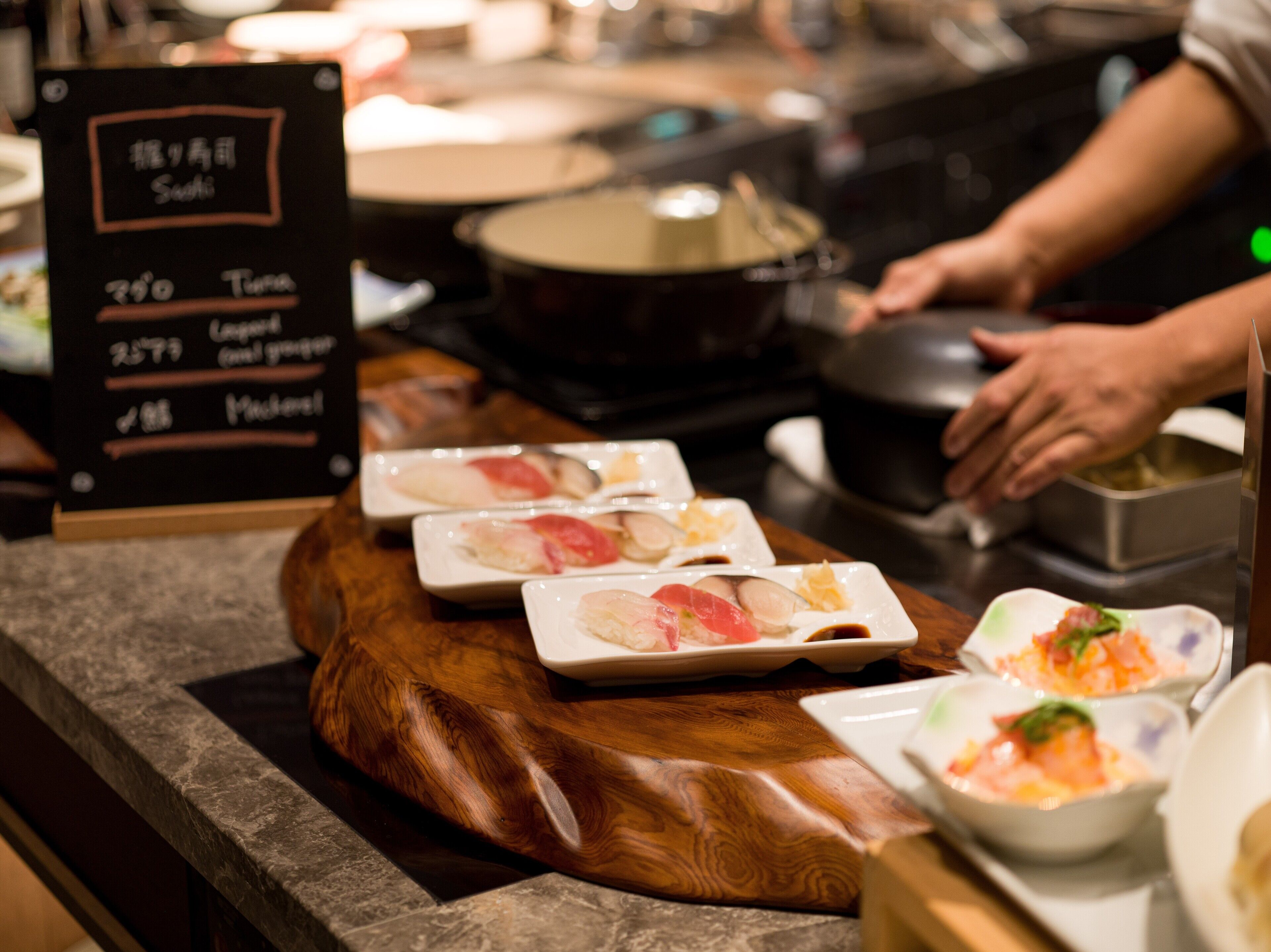 Una barra de sushi con diferentes platos expuestos en una tabla de madera y en platos.