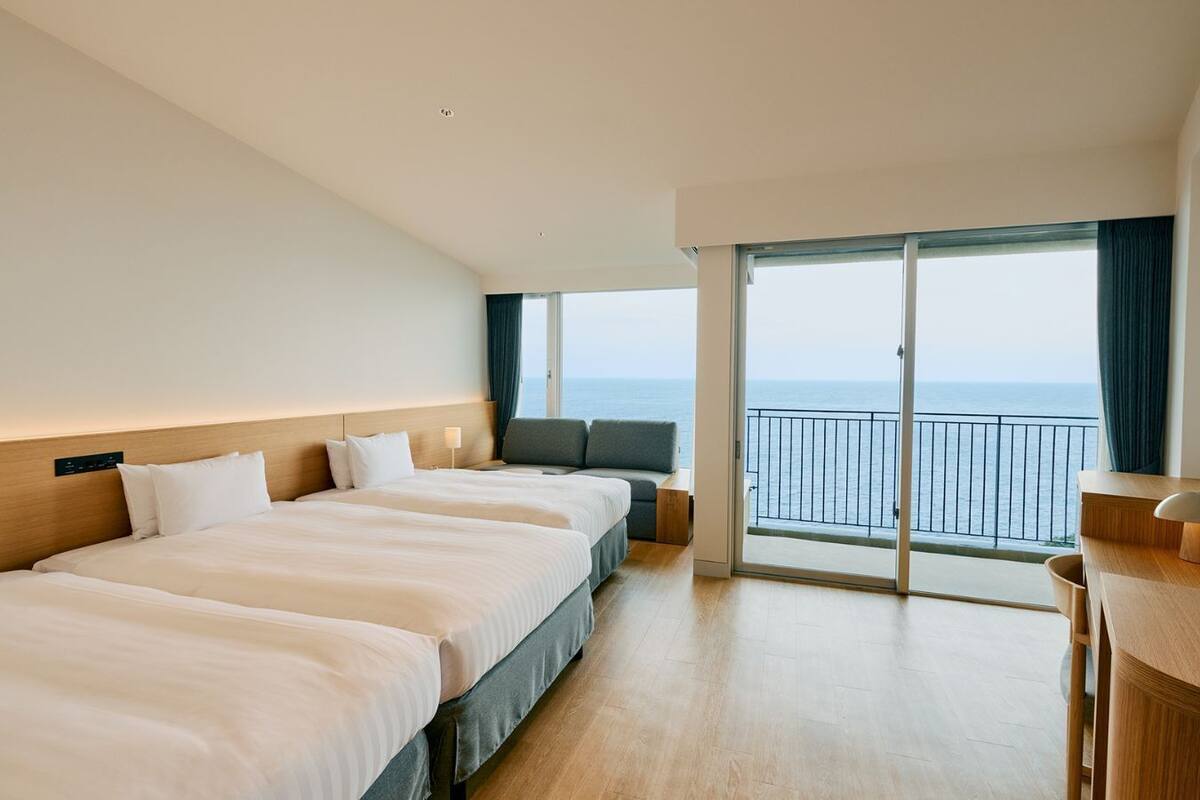 Een hotelkamer met drie bedden, een bureau en een balkon met uitzicht op zee.