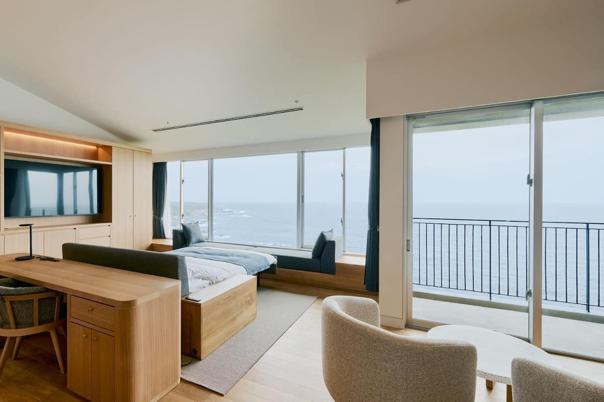 Een moderne slaapkamer met een bed, een bureau, een televisie en een balkon met uitzicht op zee.