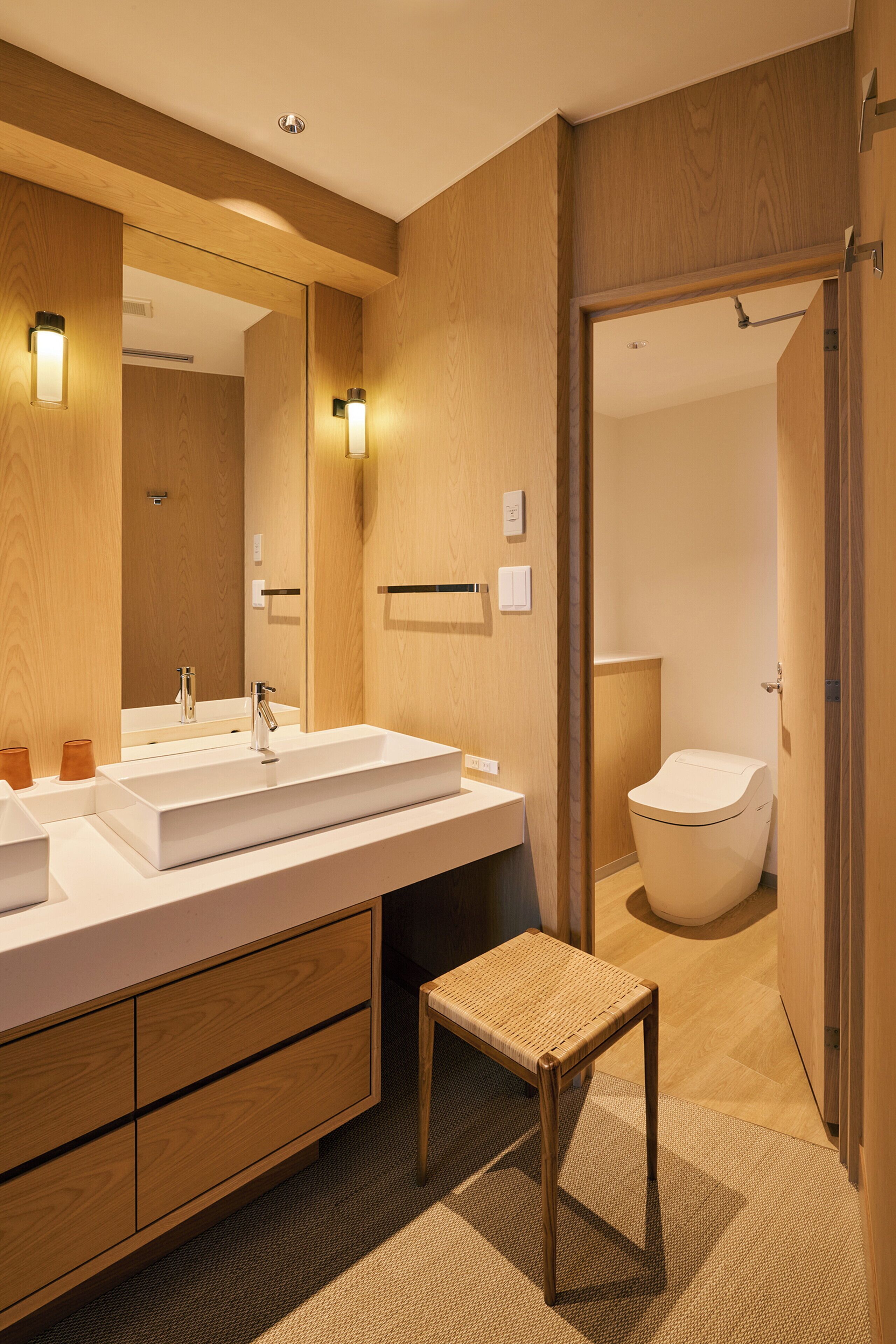Een moderne badkamer met een houten wastafelmeubel, een grote spiegel en een apart toiletgedeelte.