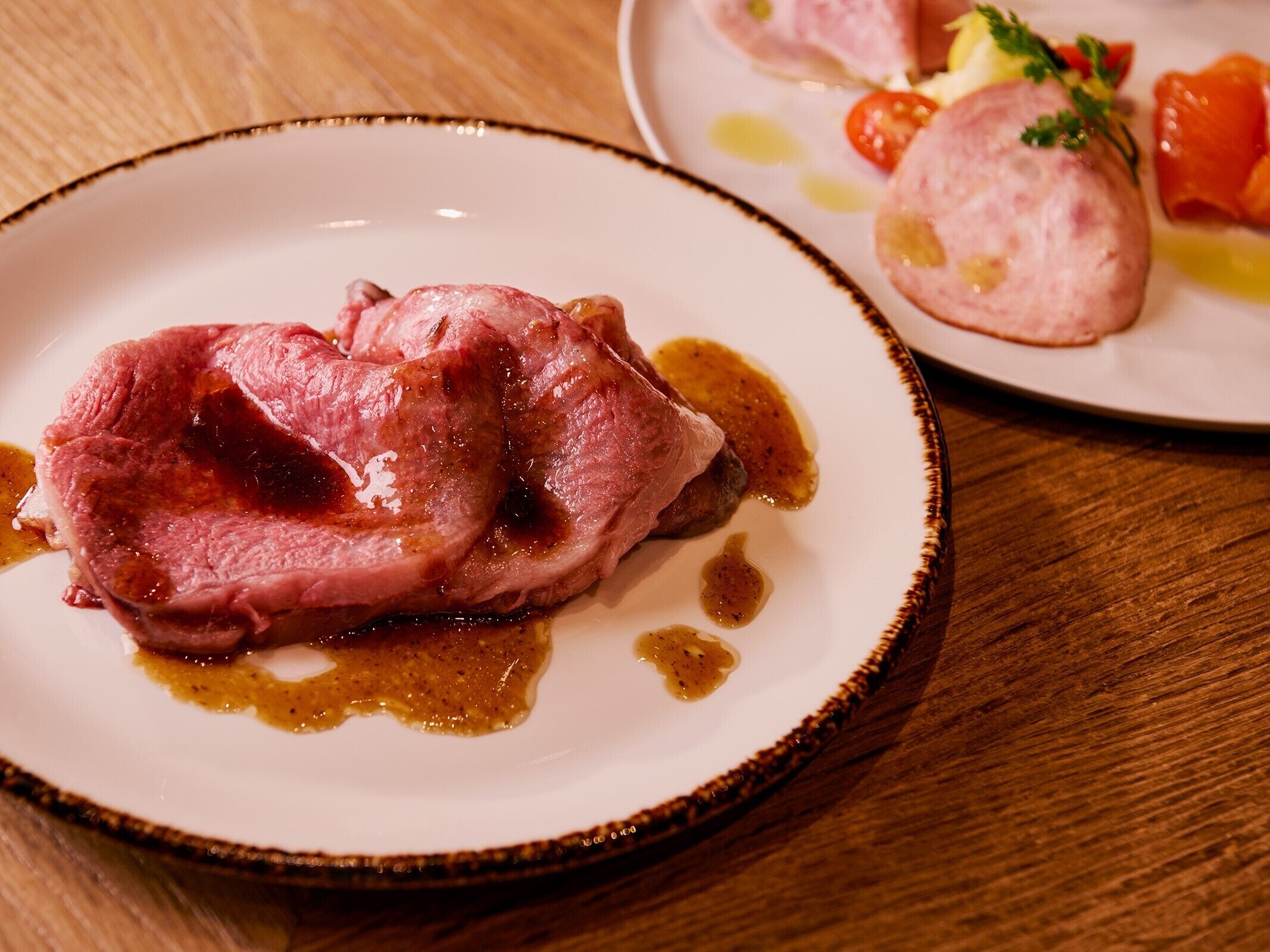 A plate with a piece of meat and sauce on a wooden table.