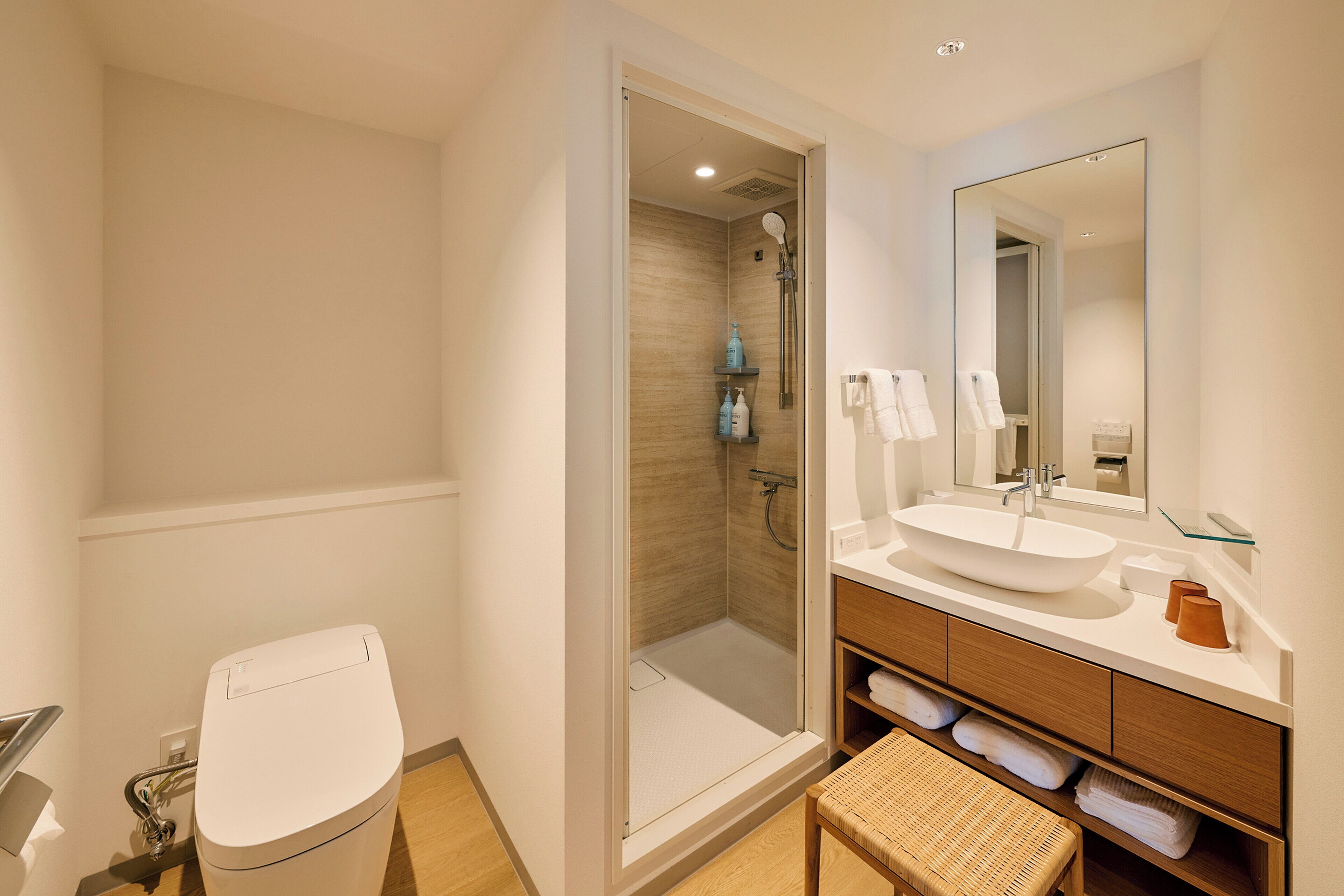 Un baño moderno con ducha envuelta en vidrio, lavamanos blanco y tocador de madera.