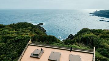 A rooftop terrace with three flat-screen TVs, overlooking a coastal landscape with rocky cliffs and dense greenery.