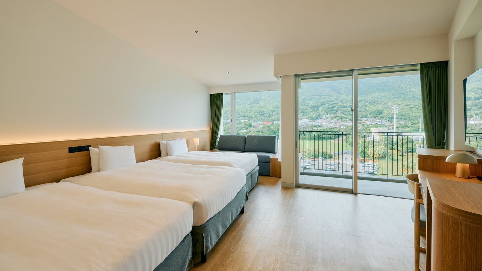 Ein Hotelzimmer mit drei Betten, einem Schreibtisch und einem Balkon mit Blick.