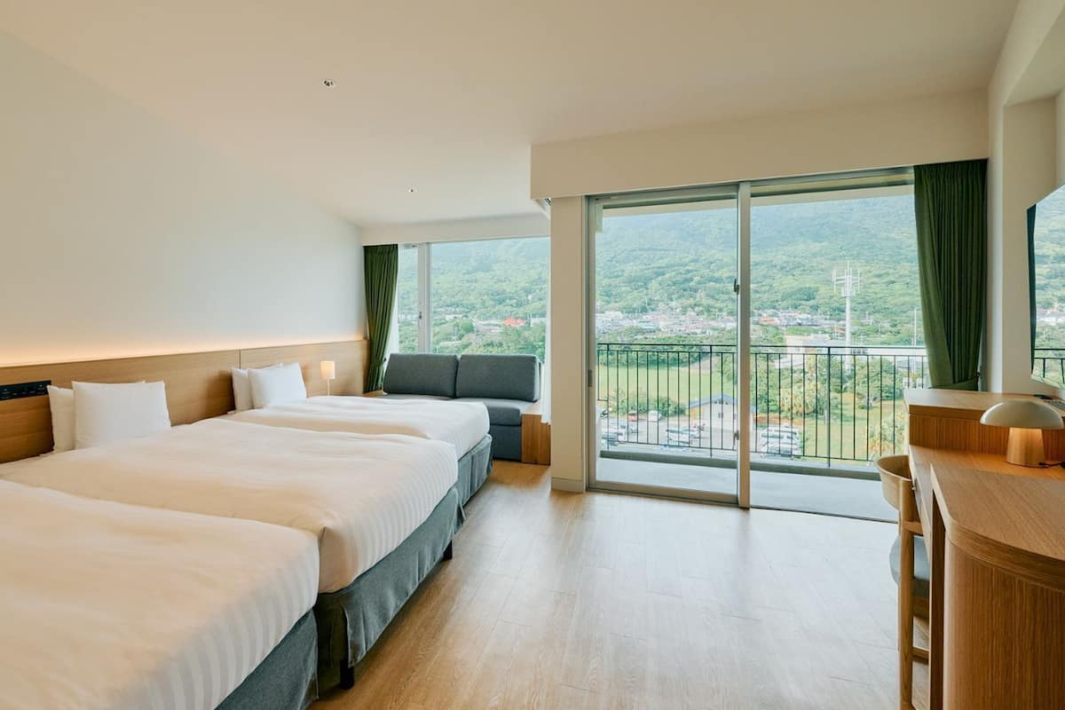 Een hotelkamer met drie bedden, een bureau en een balkon met uitzicht.