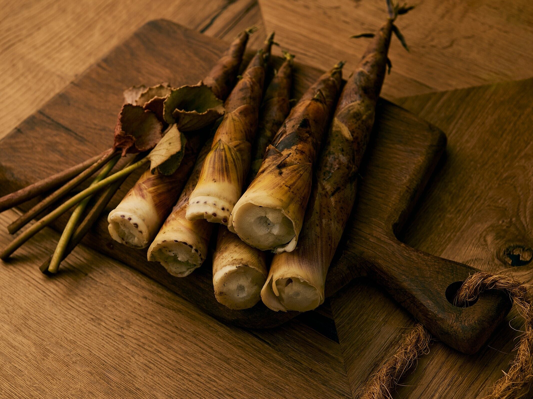 A wooden cutting board with several root vegetables and herbs on it.