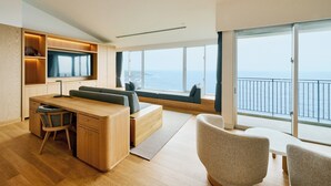 Un espace de vie moderne et décloisonné, doté d’une grande fenêtre donnant sur la mer, d’un téléviseur intégré et d’un coin salon confortable.