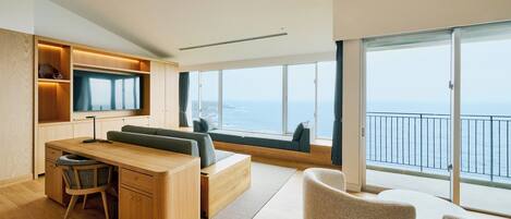 A modern, open-plan living area with a large window overlooking the sea, a built-in TV, and a cozy seating arrangement.