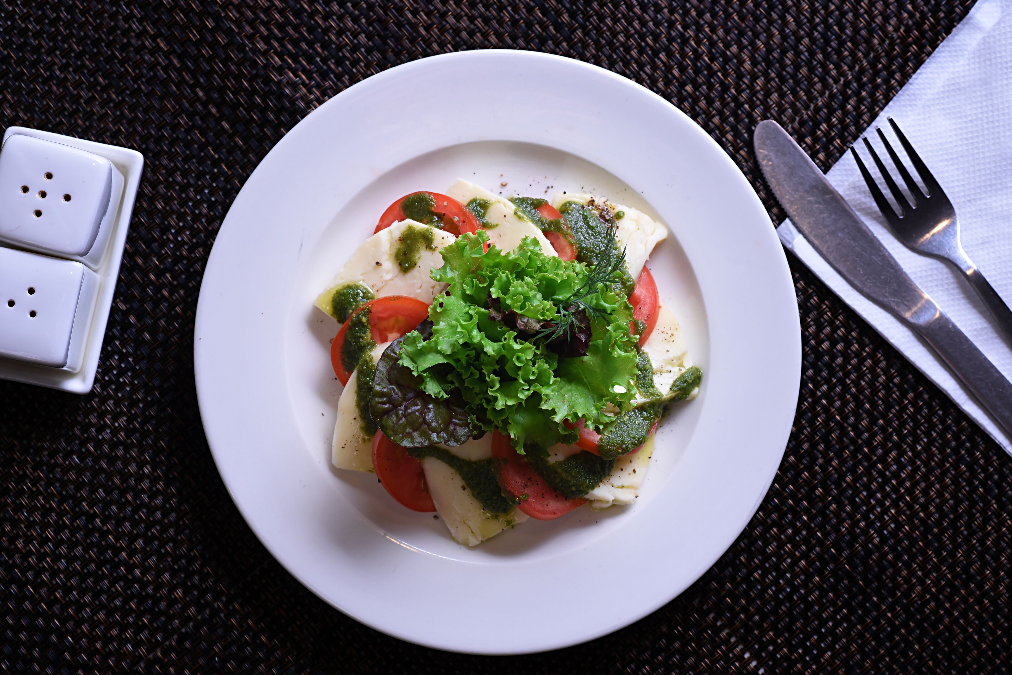 A white plate with a salad on a dark woven tablecloth.