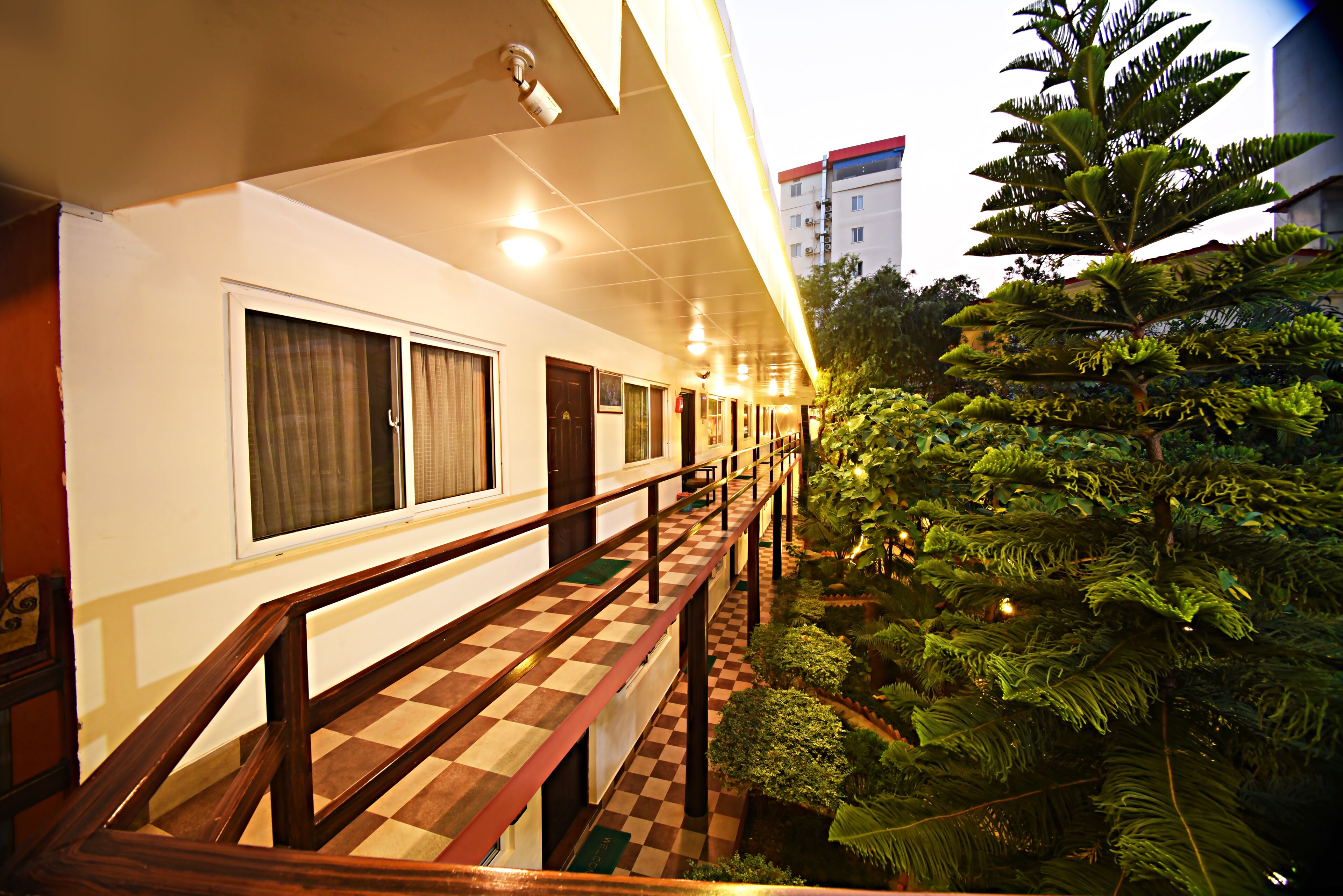A hotel corridor with a checkered floor, wooden railing, and a view of lush greenery.