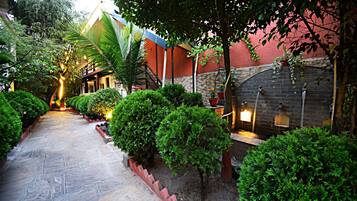 A stone pathway flanked by well-maintained bushes and a brick wall with a water feature.