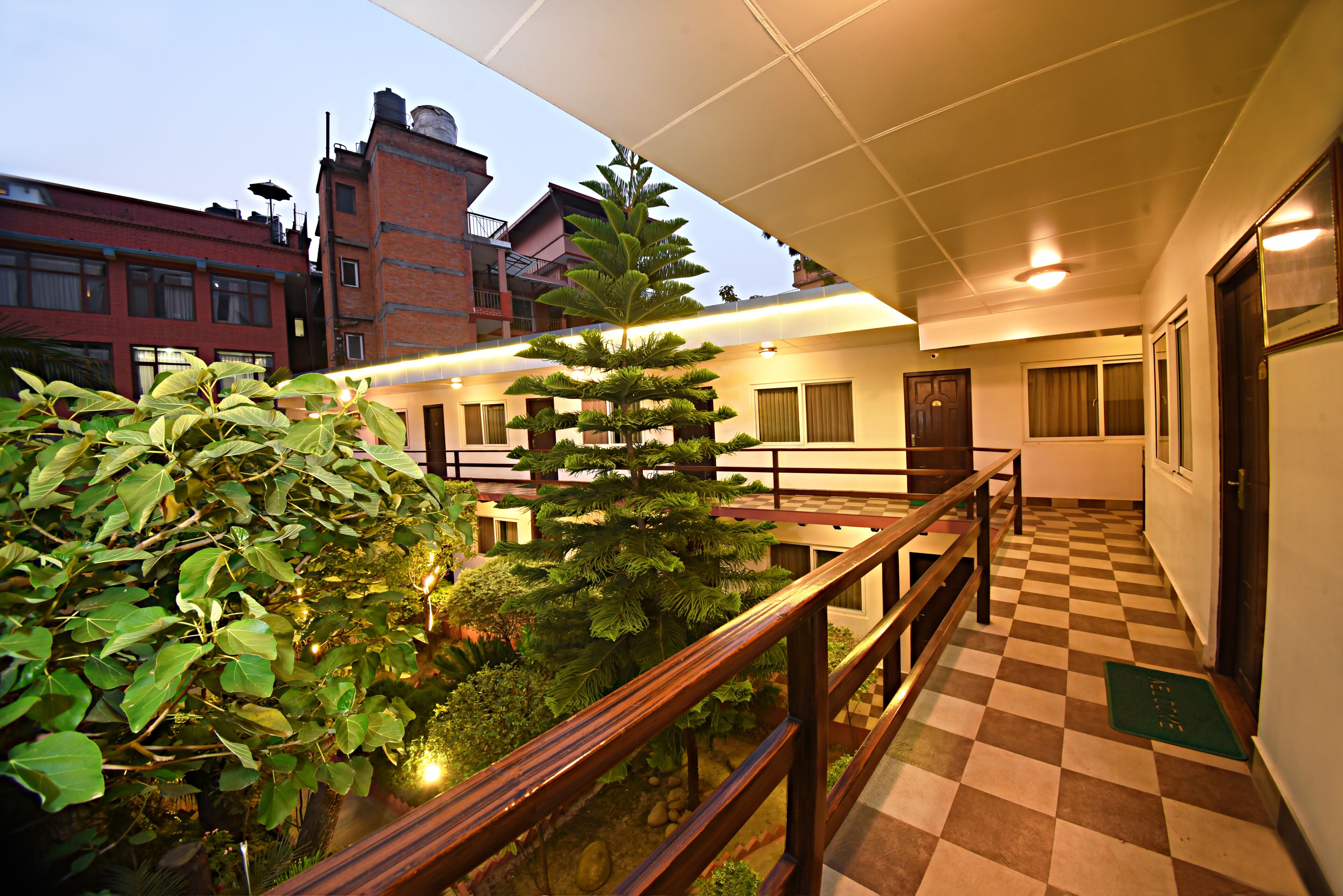 Interior de hotel con suelo a cuadros, una escalera con barandilla de madera y una planta en maceta.
