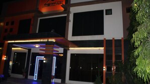 A modern hotel with a prominent orange sign, large windows, and a well-lit entrance. - Anggraeni Hotel Ketanggungan (Ketanggungan)