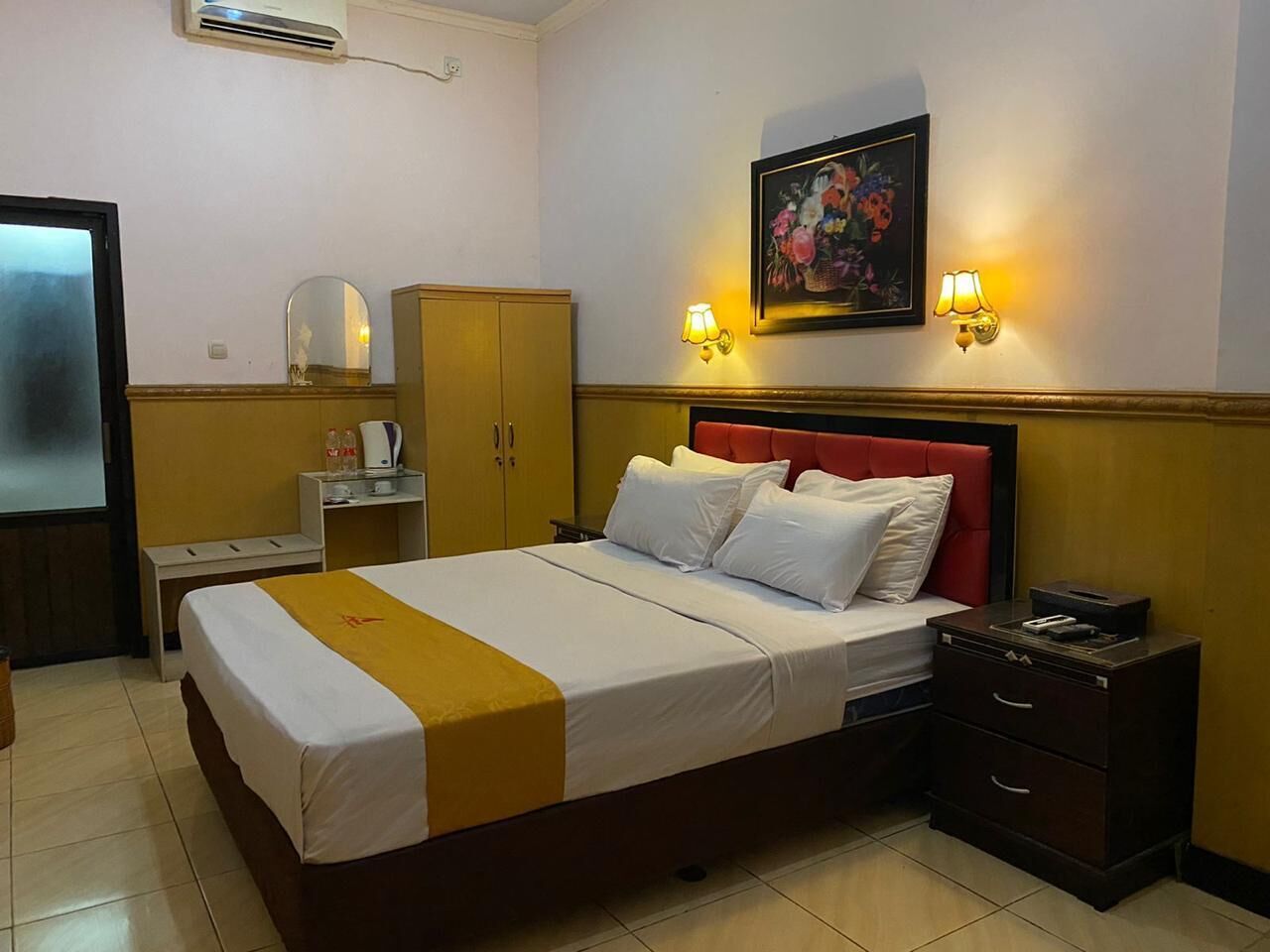 Una habitación de hotel con una cama, mesitas de noche, un armario y un cuadro colgado en la pared.
