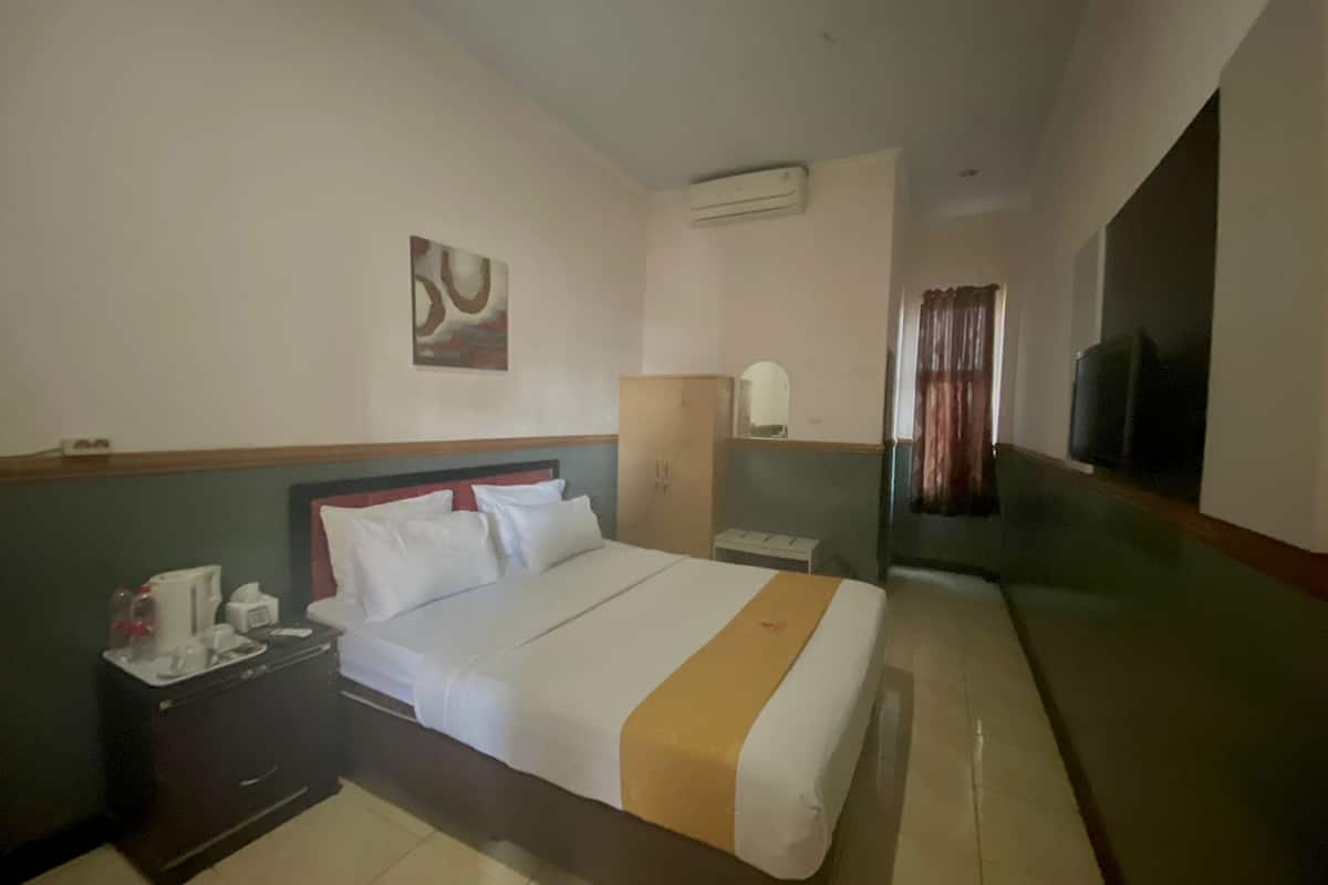 Een hotelkamer met een bed, nachtkastje met koffiezetapparaat, spiegel en televisie.