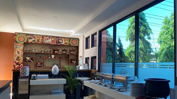 A coffee shop with a counter, shelves with coffee cups, and a large window with a view of trees. - Anggraeni Hotel Ketanggungan (Ketanggungan)