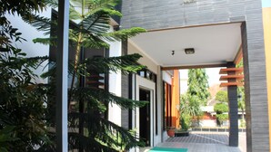 A modern building with a covered entrance, potted plants, and a tiled pathway. - Anggraeni Hotel Ketanggungan (Ketanggungan)