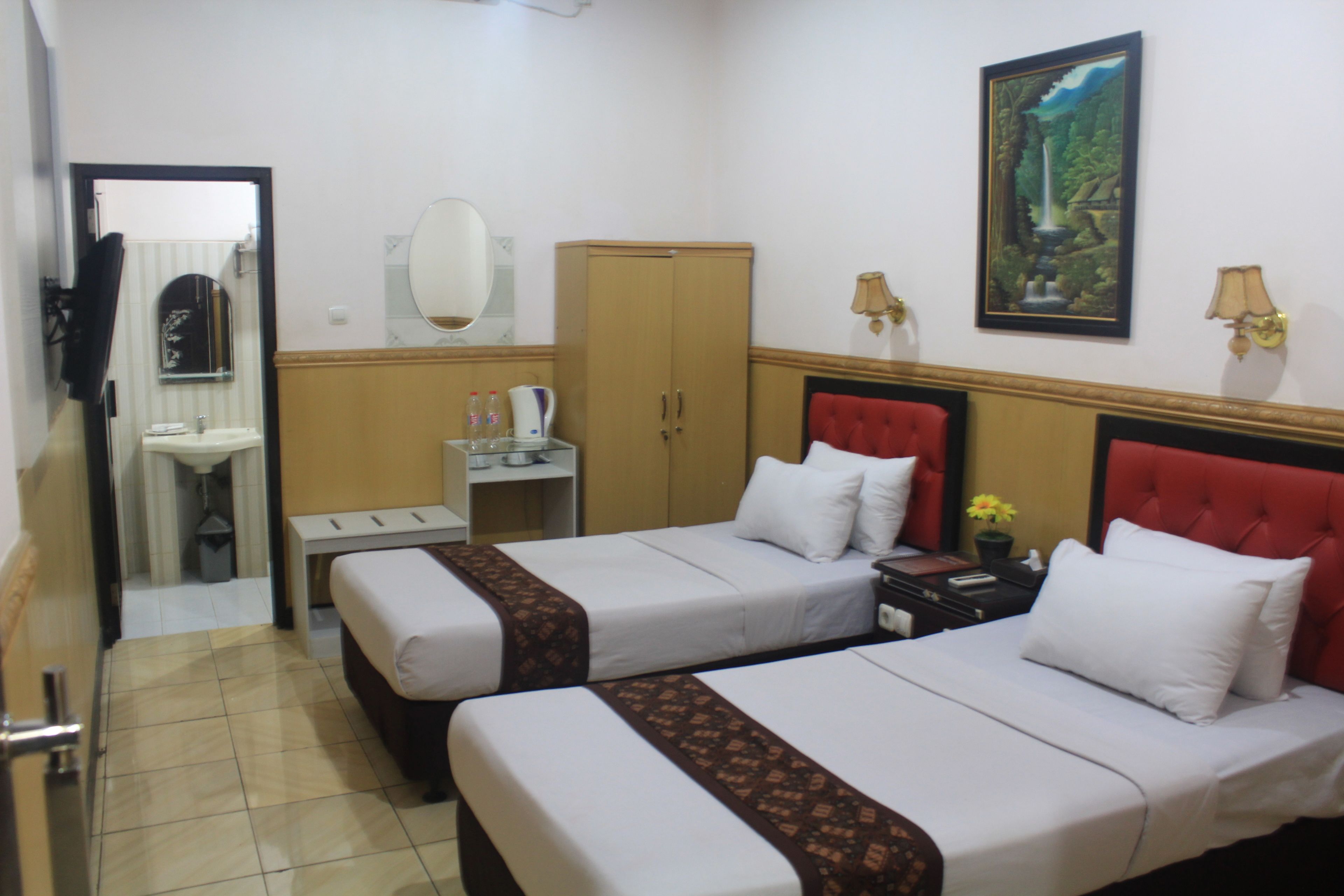 A hotel room with two beds, a bathroom, a wardrobe, and a painting on the wall.