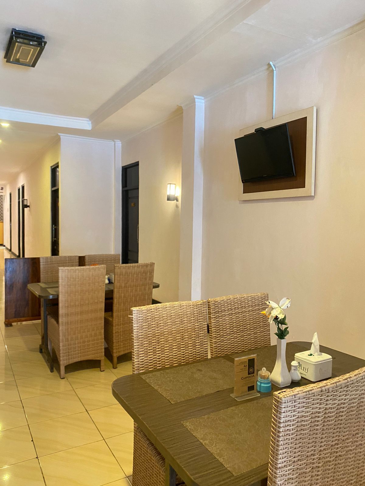 Um saguão de hotel com móveis de vime, uma TV de tela plana na parede e um balcão de recepção.