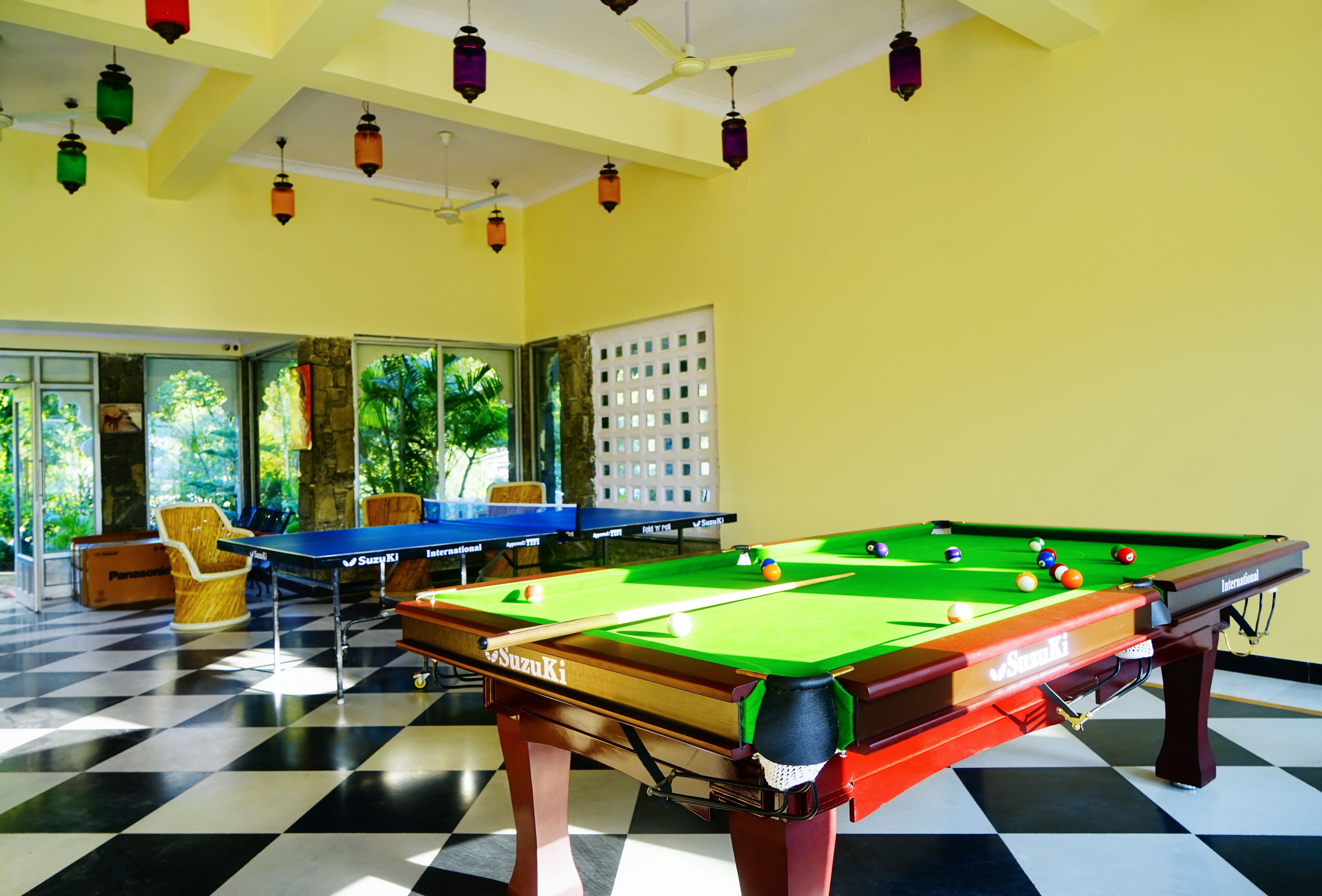A pool table with a checkered floor and a billiards table in a room with yellow walls and hanging lanterns.