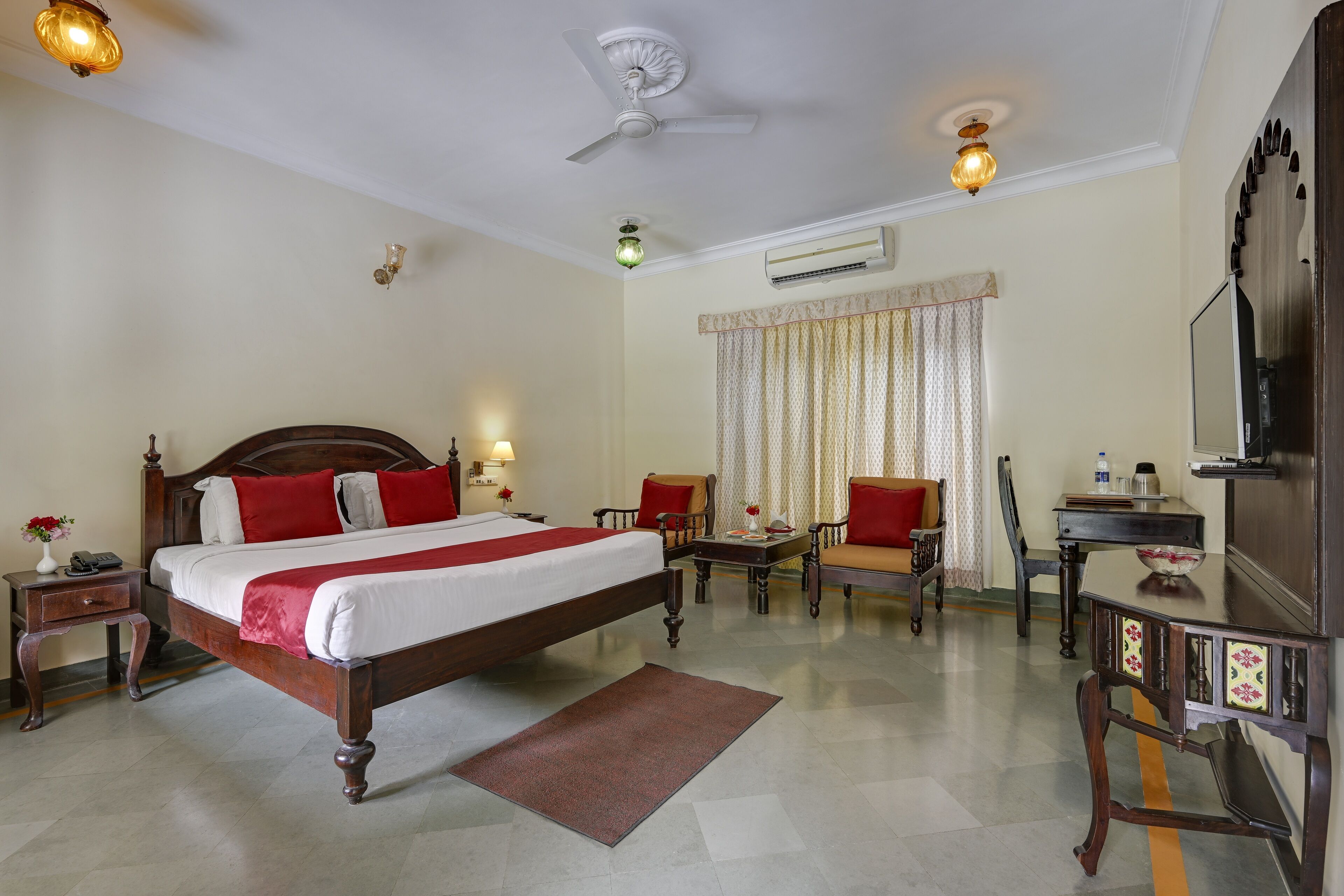 A hotel room with a large bed, a desk, a chair, a TV, and a ceiling fan.