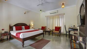 A hotel room with a large bed, a desk, a chair, a TV, and a ceiling fan.