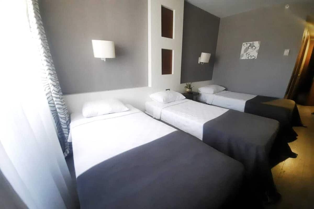 A hotel room with two beds, a bedside table, a lamp, and a wall-mounted artwork.